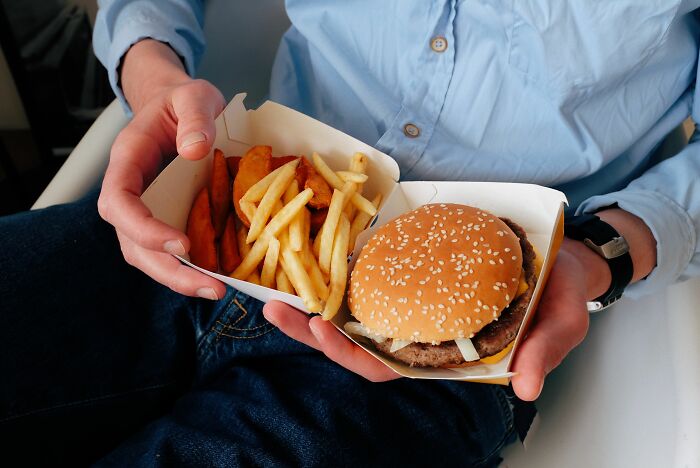 A person holds a fast-food meal with a hamburger and fries, representing an instance where someone snapped and gave in.