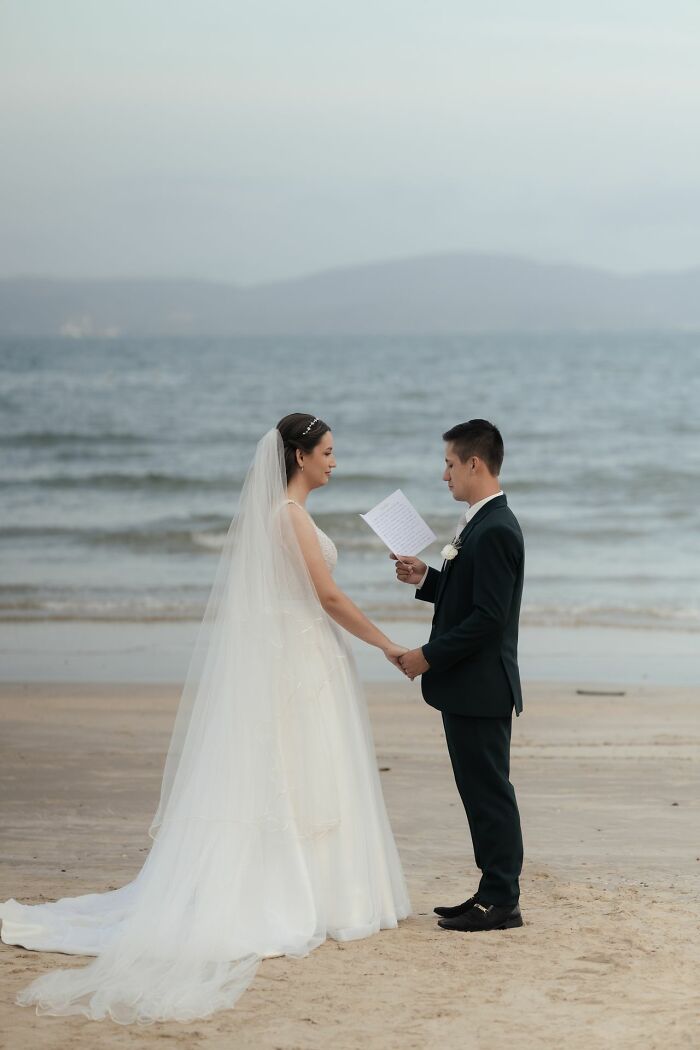 A bride and groom on a beach, holding hands and reading vows, a moment contrasting with things found on her partners phone.