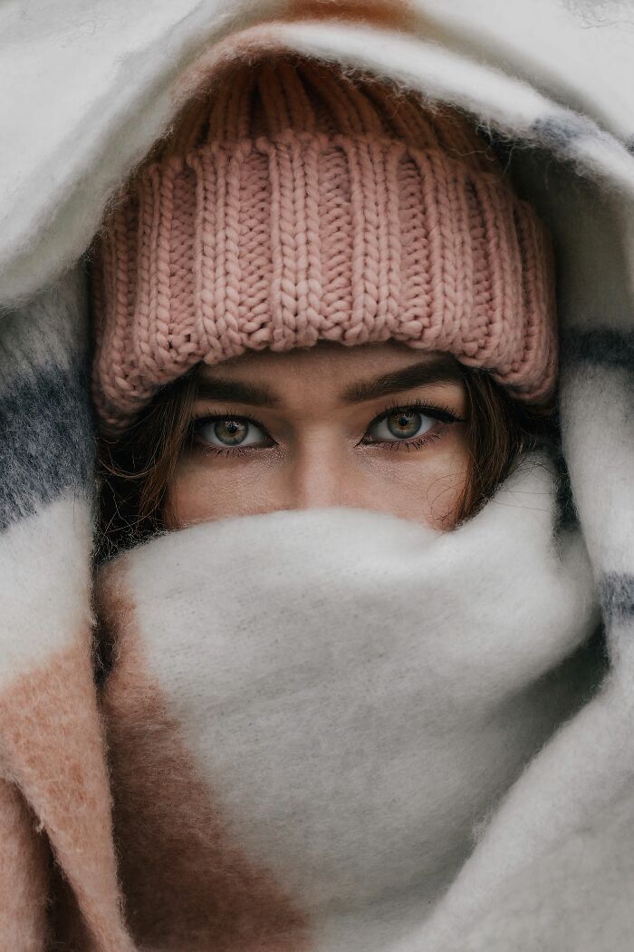 A person with a pink beanie and a blanket covering their face, revealing only their eyes, representing human bodies.