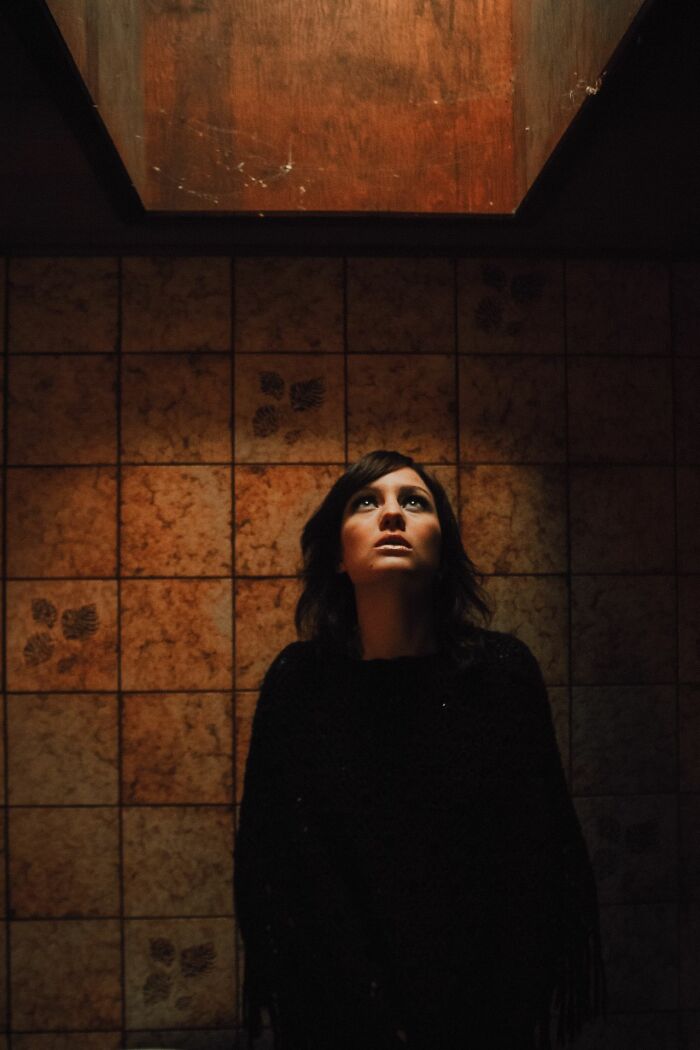 A woman looking up with concern in a dimly lit, tiled room, experiencing something she can't explain.