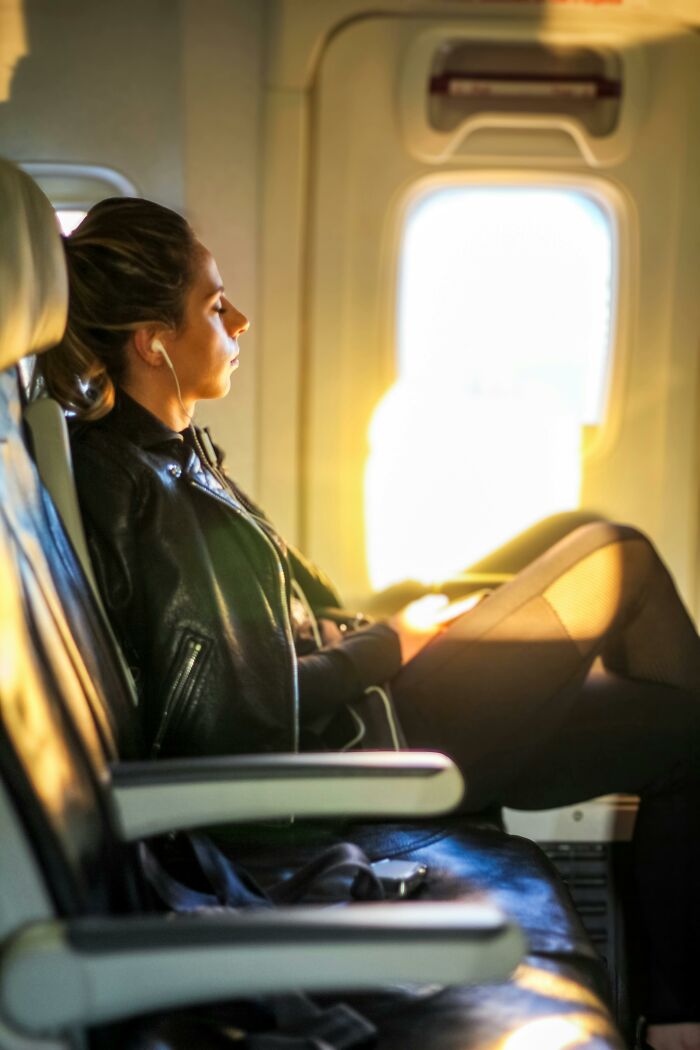Woman passenger sitting by airplane window listening to music during flight