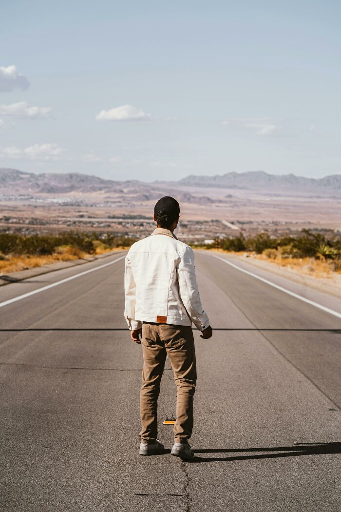 Man standing on empty road facing distant mountains