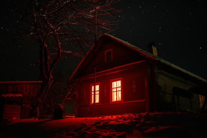 A secluded house at night, glowing red windows, hinting at an unsolved mystery under a star-filled sky.
