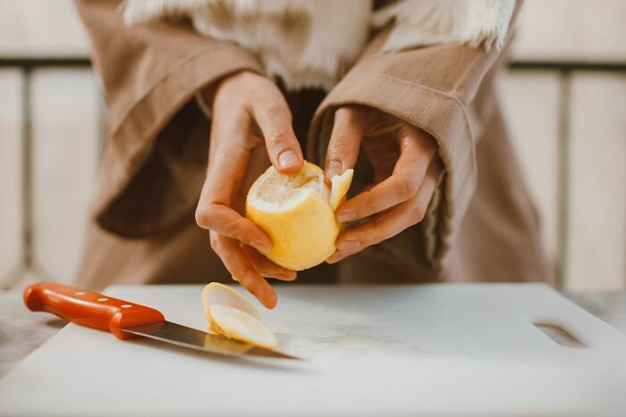 Hands struggling to peel a lemon with a knife nearby, an image conveying a challenging type of pain.