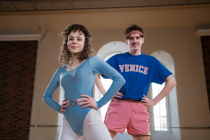 A woman in a blue leotard and a man in a Venice t-shirt posing, representing 80s & 90s references.