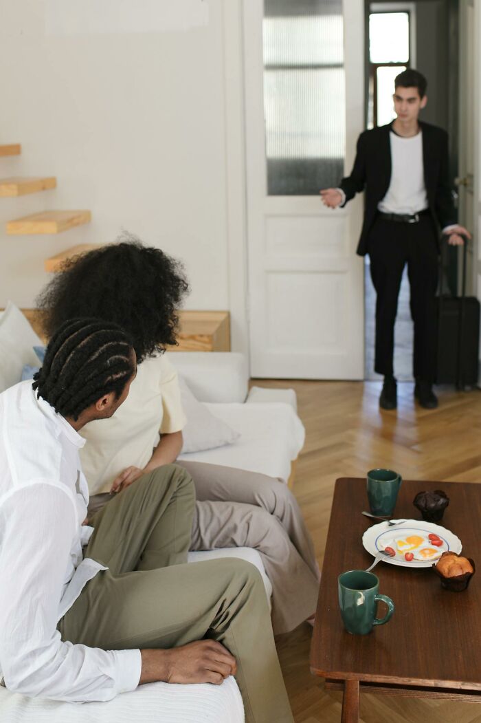 Couple confronting man with suitcase over infidelity in living room