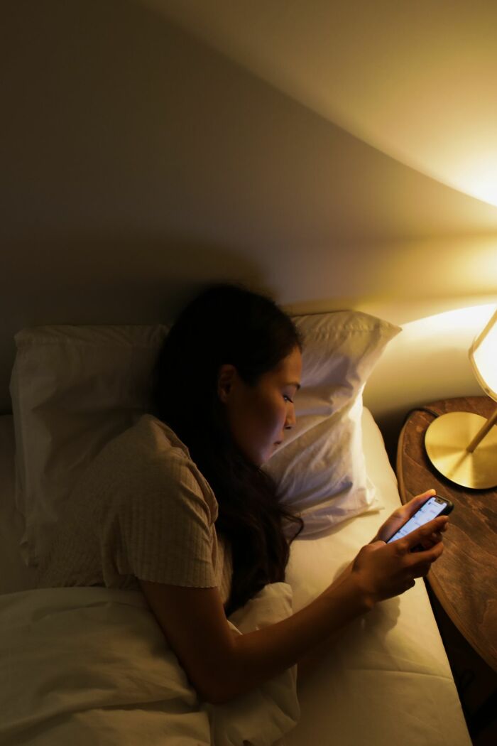 A woman secretly looking at her partner's phone in bed, finding the worst things.