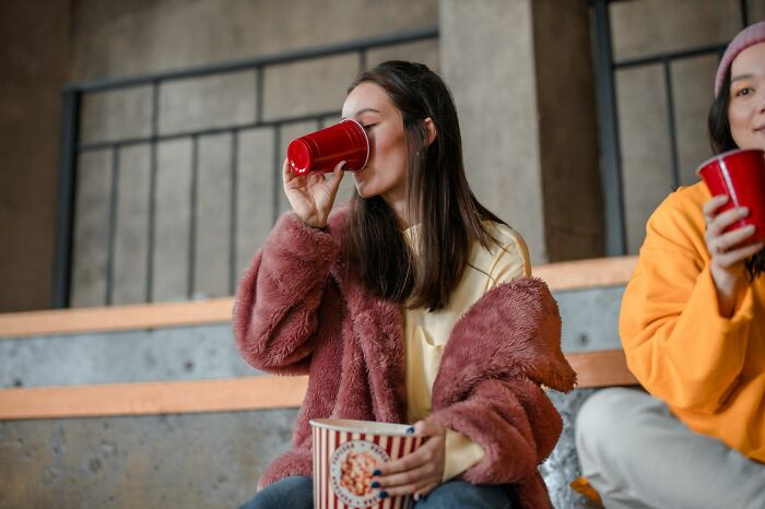Woman drinking from red cup while holding popcorn at event