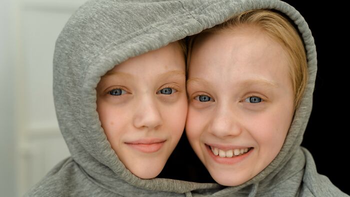 Two young doppelgangers wearing gray hoodies smiling close together Two young doppelgangers wearing gray hoodies smiling close together