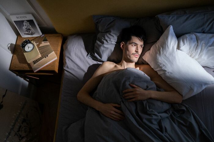 A man lies awake in bed, experiencing an unexplainable feeling of the bed compress, a mysterious experience.
