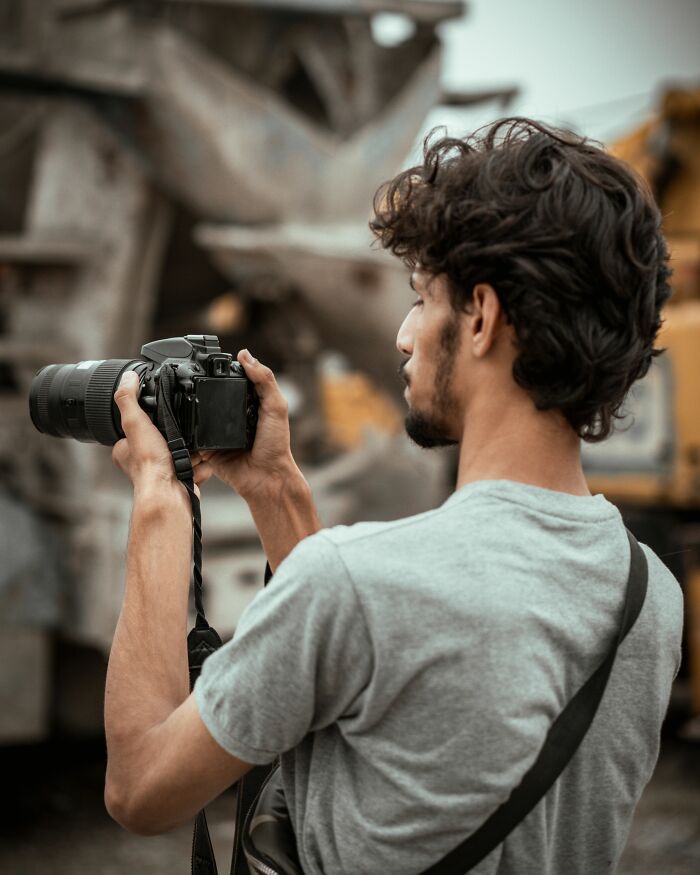 A man with curly hair holding a camera, suggesting capturing stories about people who hid their true selves.