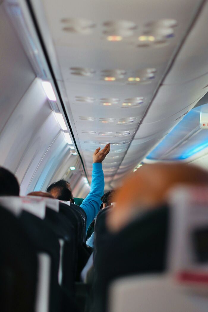 Passenger reaching to open overhead compartment inside airplane