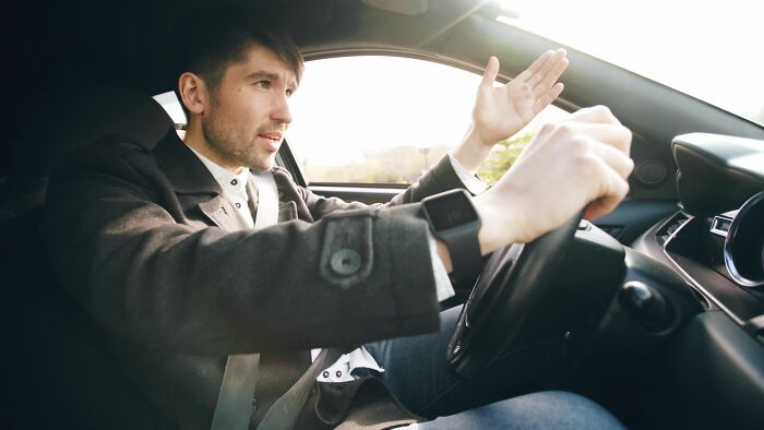 A man driving a car, looking frustrated and gesticulating, hilariously misread social cues causing an awkward situation.