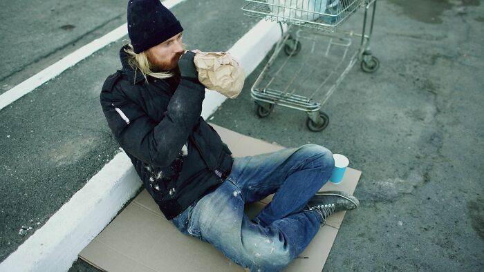 A homeless person sitting on the ground, breathing into a paper bag, highlighting the struggles of hidden true selves.
