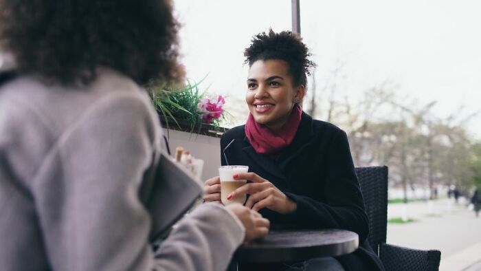 Two women smiling and chatting over coffee, subtly revealing hints that a person is secretly very smart.
