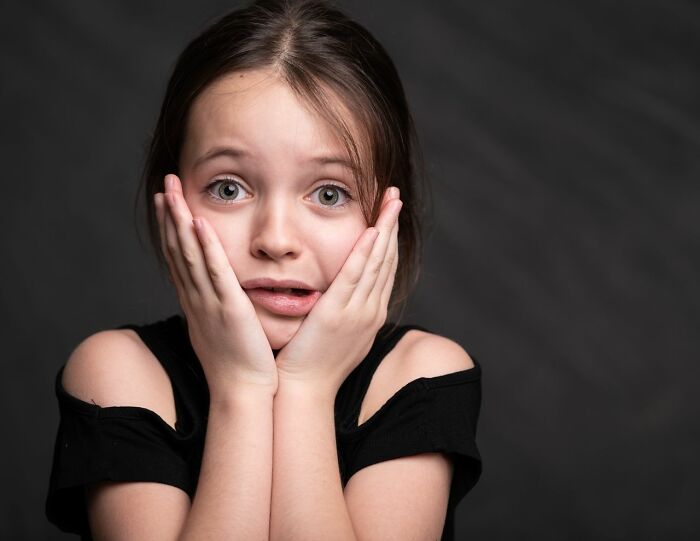 A young girl with wide eyes and hands pressed to her cheeks, expressing surprise about experiences people can't explain.