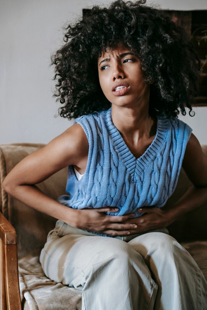 Woman with curly hair clutching her stomach in pain, representing facts about human bodies and health.