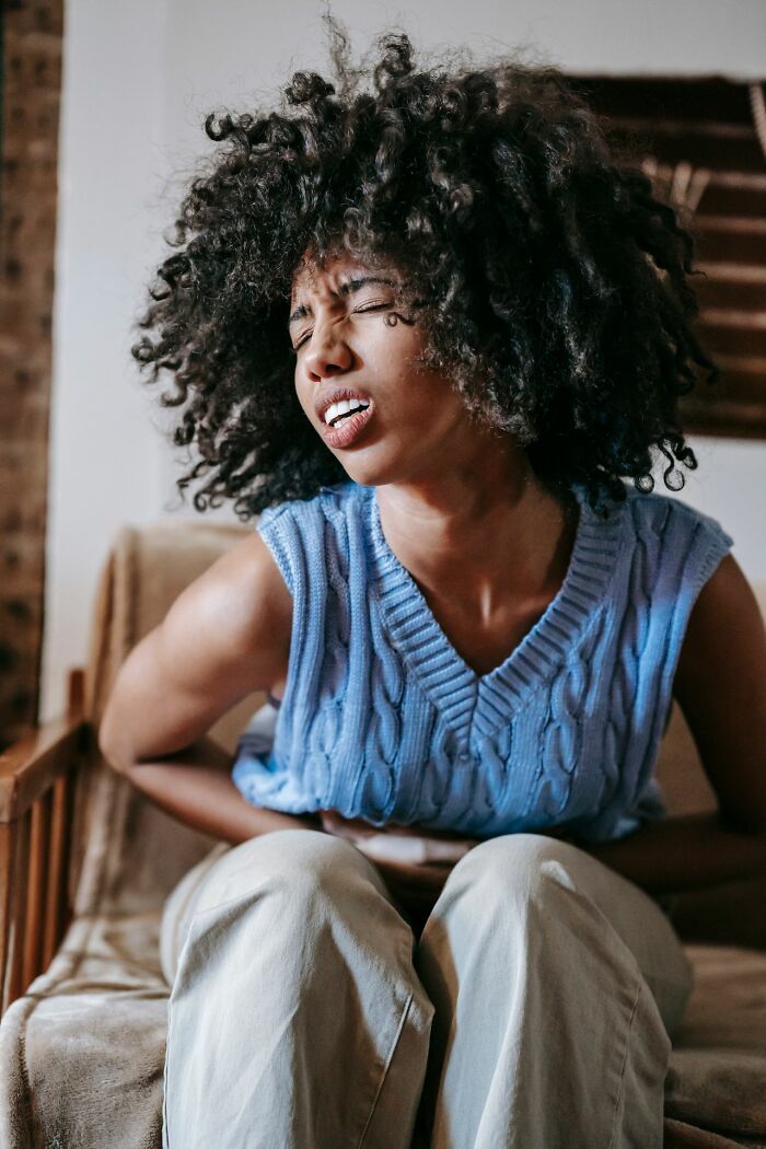 A woman sitting with her eyes closed in pain, clutching her stomach.