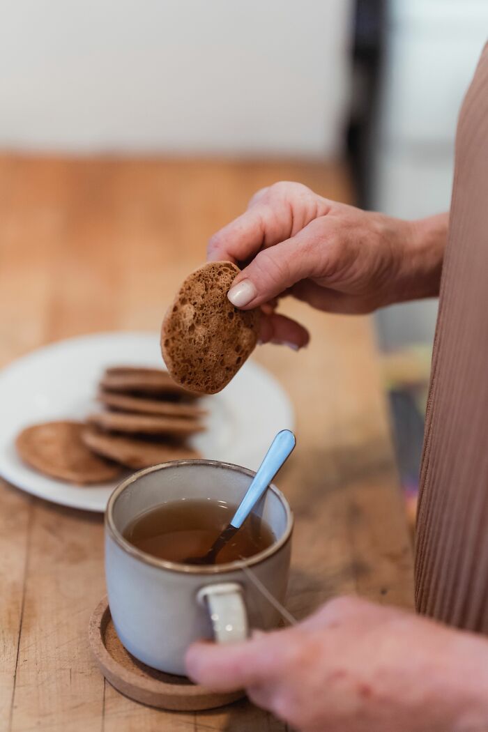 Hand dipping biscuit into a cup of tea on a wooden table