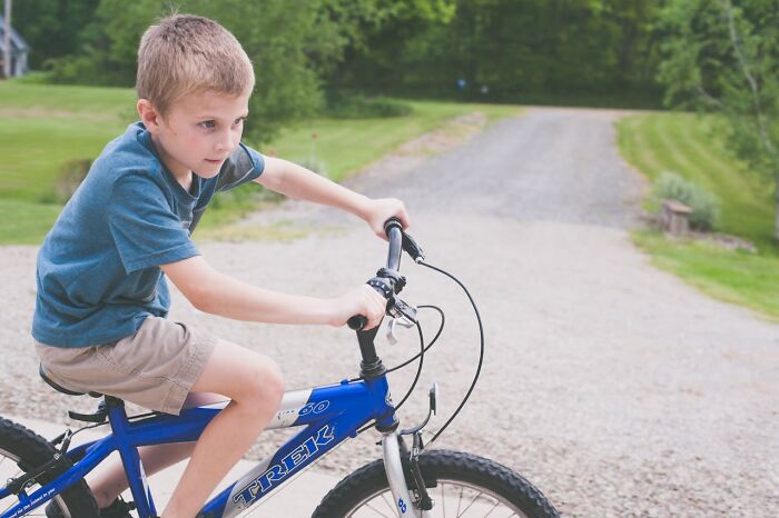 Young boy riding blue bike outdoors on gravel pathway