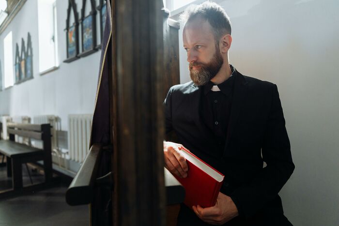 Thoughtful priest sitting in church holding book reflecting on family secrets