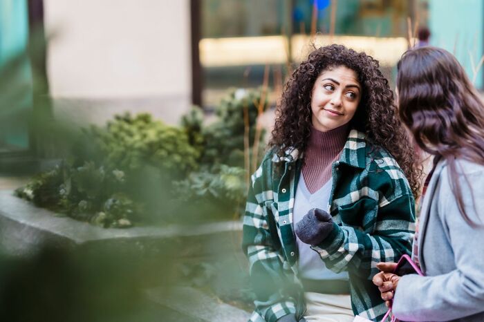 Two women talking outdoors, one with curly hair, demonstrating hints that a person is secretly very smart.