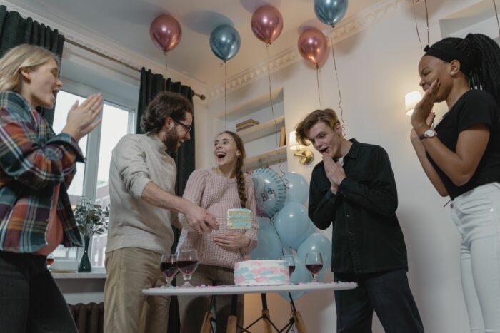 Group celebrating gender reveal party cutting cake with pink and blue decorations Group celebrating gender reveal party cutting cake with pink and blue decorations