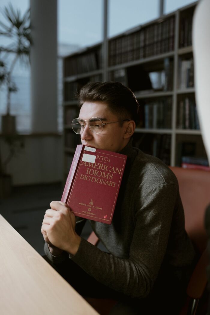 A man in glasses holding a dictionary to his face, reflecting on hints that show a person is secretly very smart.