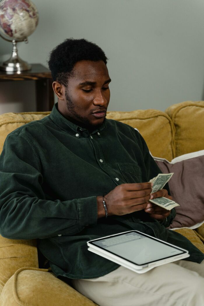 Man counting cash while seated with tablet on lap