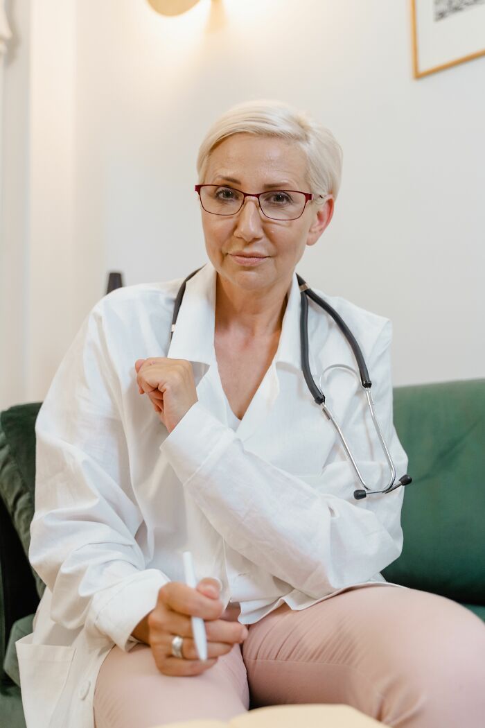 A medical professional, possibly a doctor, sits looking at the camera, misreading social cues. Her expression is serious.