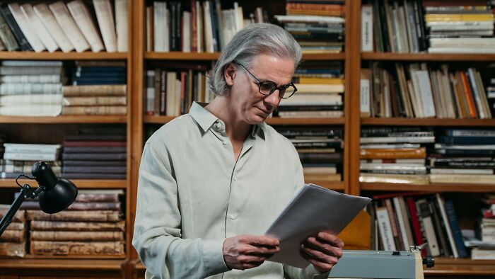 A well-rounded person reads documents in a library, surrounded by bookshelves filled with various general knowledge books for a quiz. A well-rounded person reads documents in a library, surrounded by bookshelves filled with various general knowledge books for a quiz.