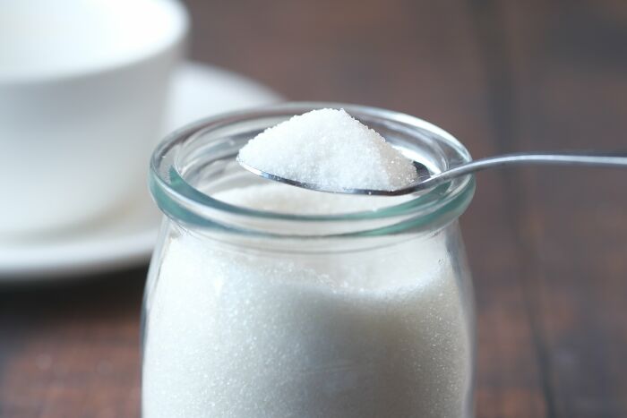 Sugar in a glass jar with a spoonful above it close-up