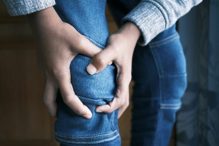 A person in jeans clutching their knee, illustrating pain often experienced during ER visits.
