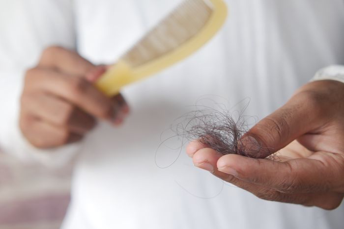 Close-up of a person holding a clump of hair in one hand and a comb in the other, symbolizing hair loss.