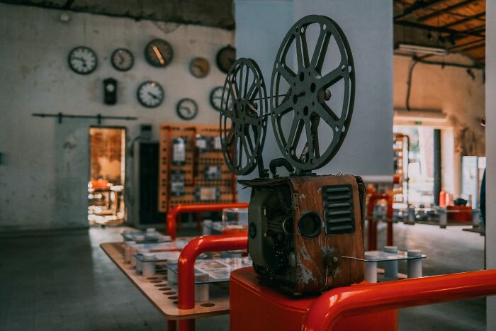 A vintage film projector, central in a room with a white wall adorned with various clocks and film-related items, evokes famous films.