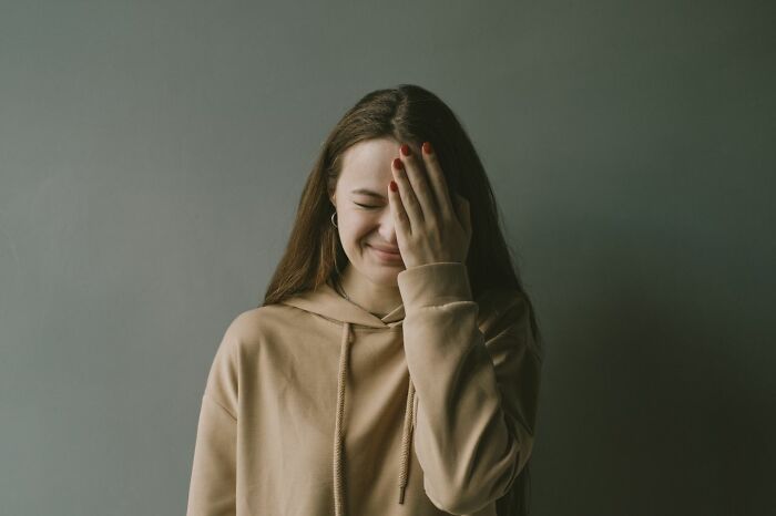 A young woman covering her face, laughing or embarrassed, reflecting unserious ER visits.