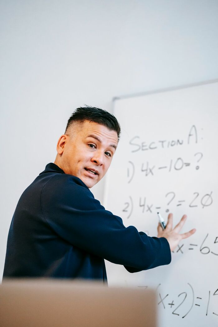 A man pointing to a whiteboard with math problems, showing hints of being very smart.