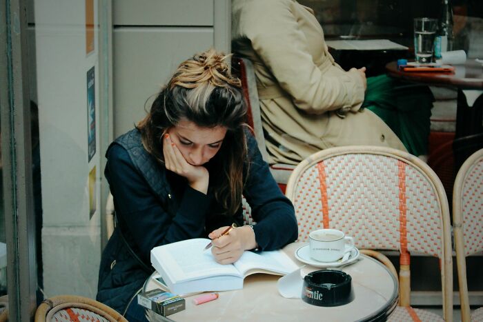 A young woman in a cafe, engrossed in a book and writing, surrounded by misheard phrases and common language errors. A young woman in a cafe, engrossed in a book and writing, surrounded by misheard phrases and common language errors.