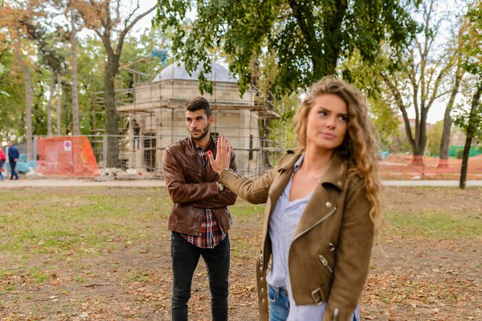A woman making a stop gesture to a man in a park, representing mens turn-offs.