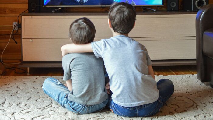 Two boys watching Saturday Morning Cartoon trivia from the 1960s to the 2000s on TV, sitting on a rug.