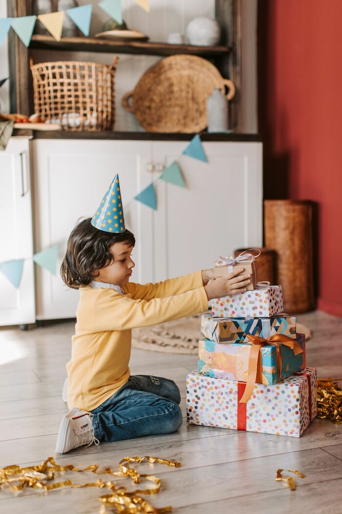 Child with party hat stacking birthday presents on floor