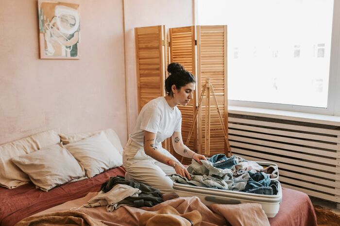 Woman packing suitcase in bedroom after discovering partner's phone secrets