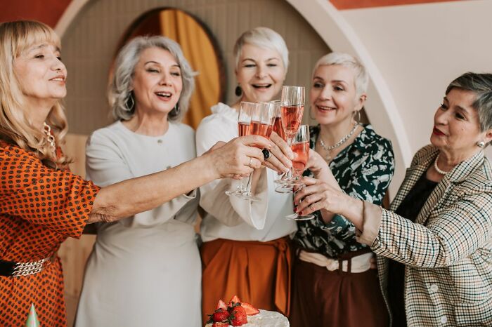 Five smiling women toasting with pink champagne, celebrating and sharing stories from polygamist families.