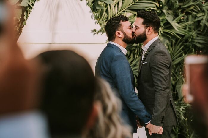 Two men in suits sharing a kiss at their wedding, symbolizing crazy but true facts like Wyoming only having two escalators.