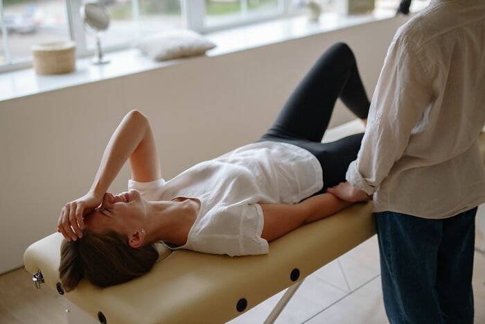 A woman lies on a medical table, holding her head, potentially misreading social cues from a therapist or during a session.