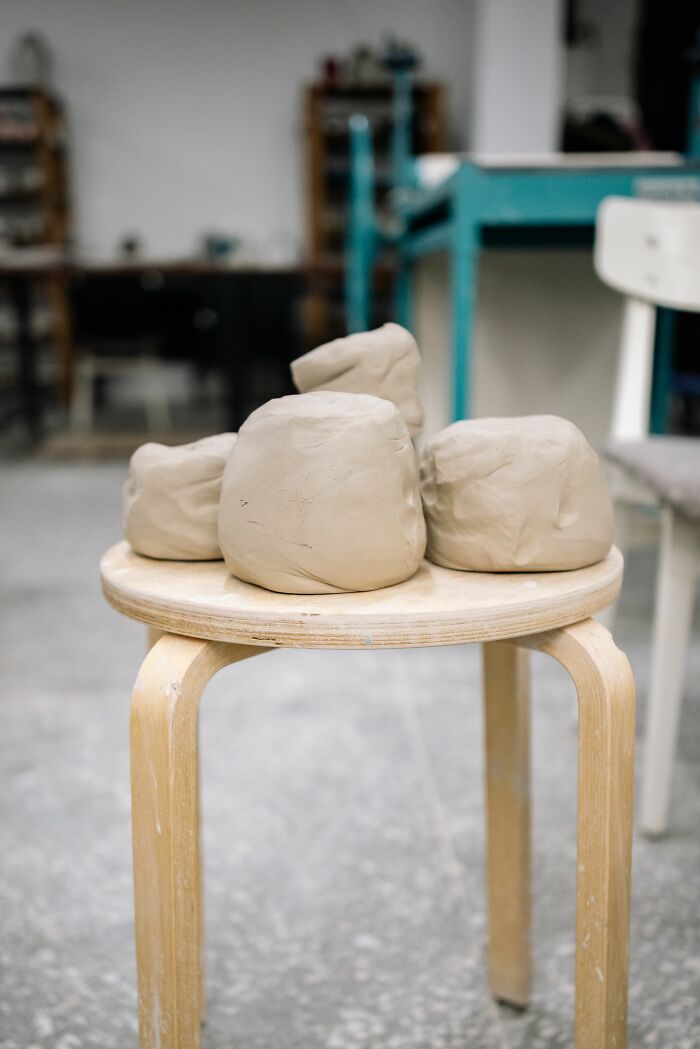 Several lumps of light-colored clay are stacked on a wooden stool in a studio. People hid their true selves.