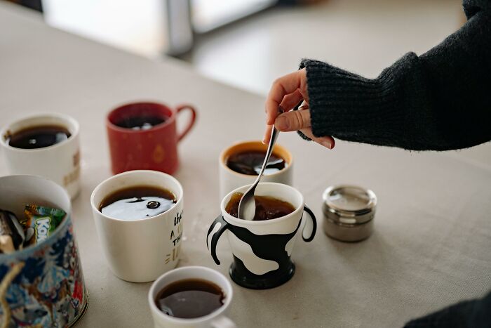 Hand stirring tea in a mug among several cups on a table