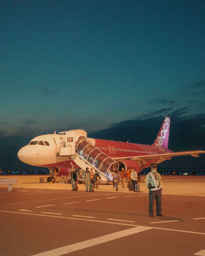 Passengers disembarking from a plane on the runway at night with airport staff nearby