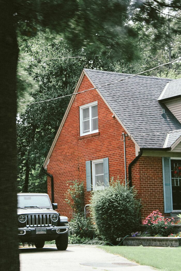 A red brick house with green shutters and a car parked in front, representing lives where people hid their true selves.