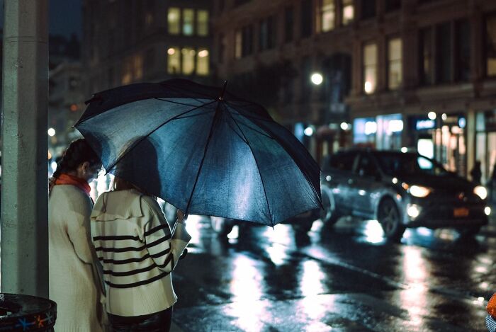 People experiencing something creepy on a rainy city street at night, with an umbrella glowing.
